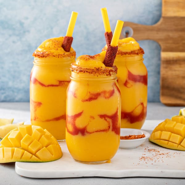 Three El Azteca Mexican mango smoothies with chamoy, chili-lime seasoning, and mango chunks.
