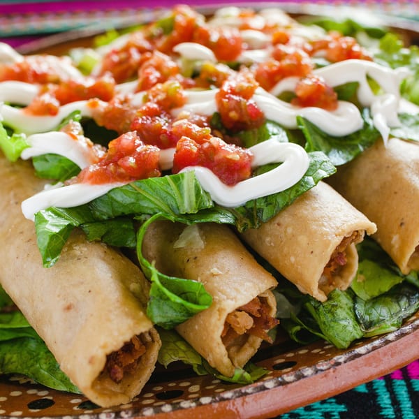 Crispy El Azteca Mexican taquitos on a bed of lettuce, topped with salsa and sour cream.